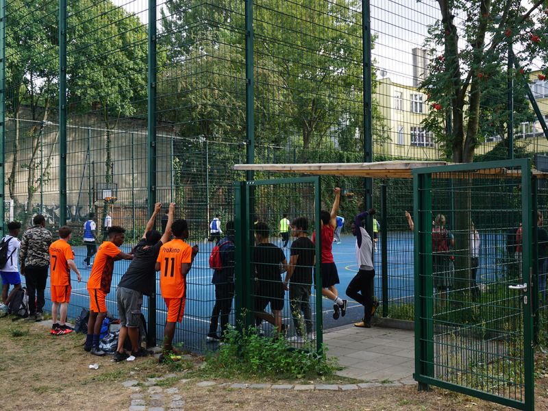 Kinder gucken von außen den Kickenden im Käfig zu