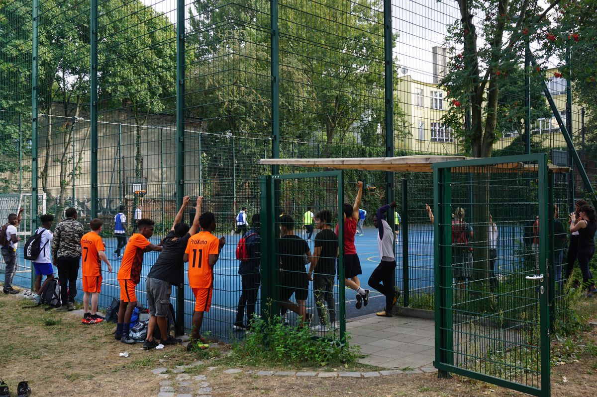 Kinder gucken von außen den Kickenden im Käfig zu